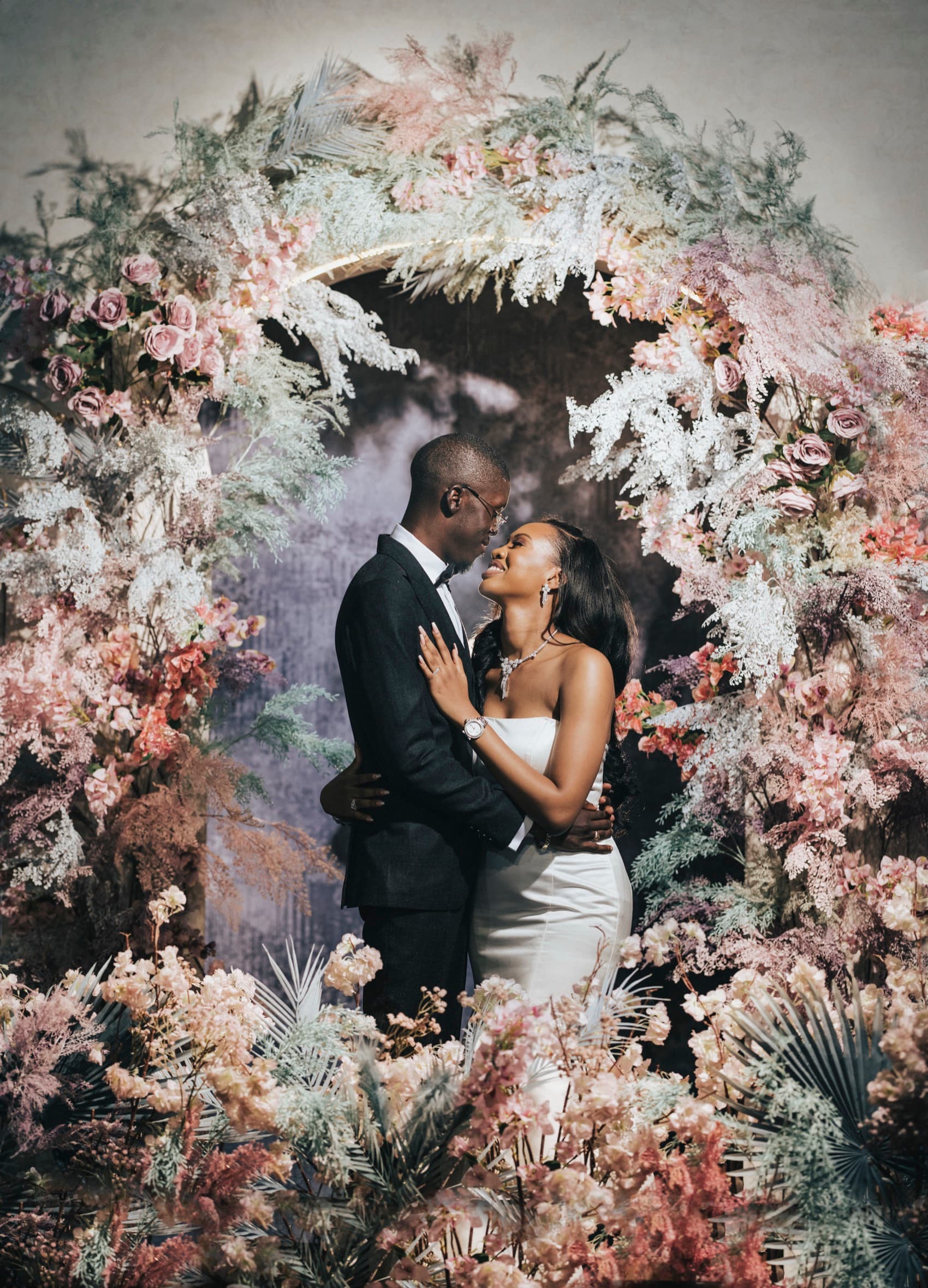 Ore and Esi's white-wedding ceremony beneath a tall floral arch.